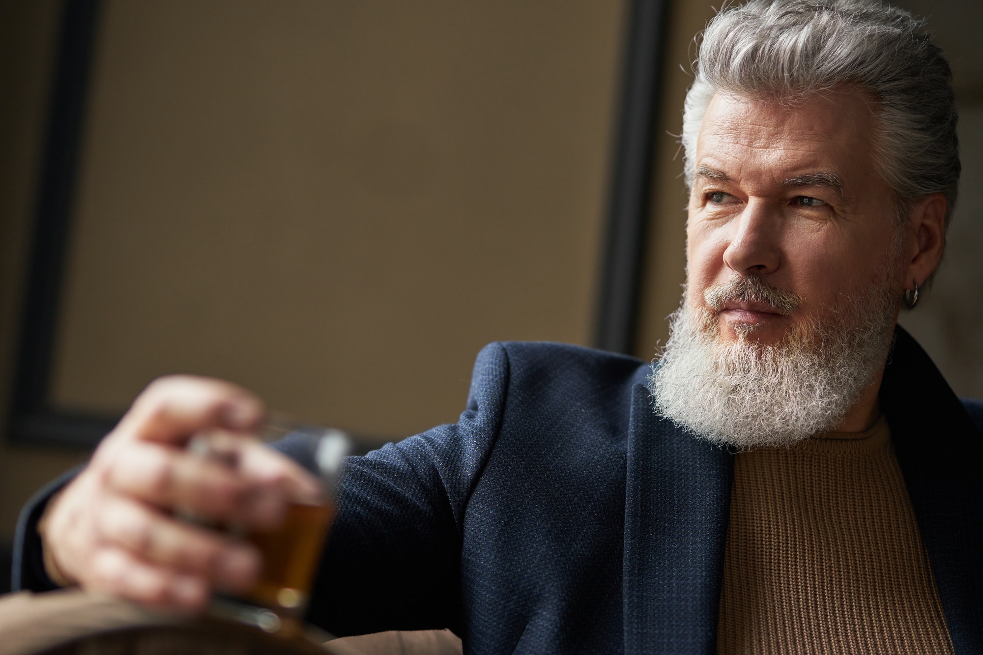 Confident middle aged business man holding glass of alcohol scotch whiskey in his hand while